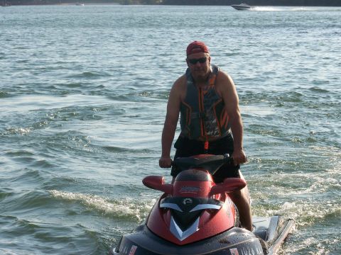 2006 Sea-Doo 230 Wake - A man rides a red jet ski on the water, with another boat visible in the background.