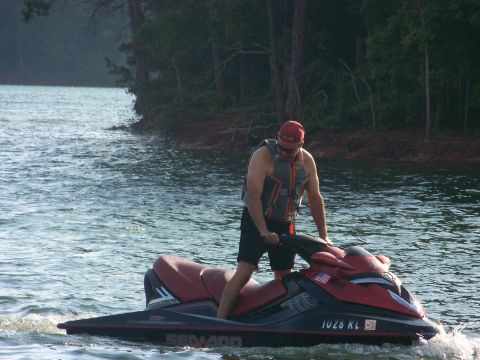 2006 Sea-Doo 230 Wake - Rider on a 2006 Sea-Doo 230 Wake jet ski on a lake, with trees in the background.