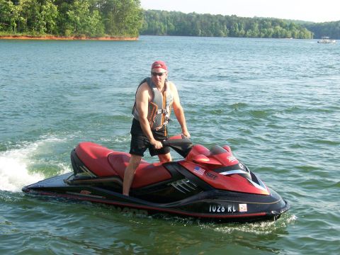 2006 Sea-Doo 230 Wake - A man in a life vest rides a jet ski on a lake with trees in the background.
