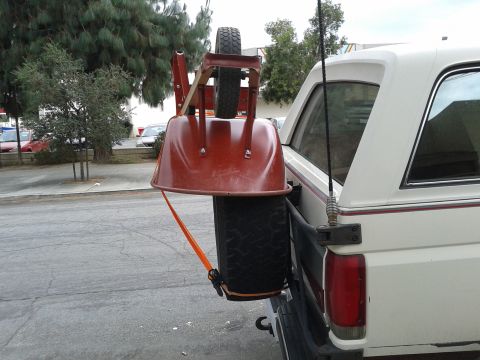 1990 Ford Bronco - A wheelbarrow and spare tire are secured to the rear of a white truck.