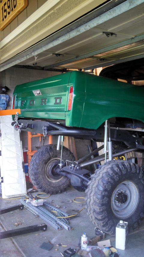 1967 Ford F-250 - Rear view of a green 1967 Ford F-250 pickup truck, lifted and undergoing maintenance.