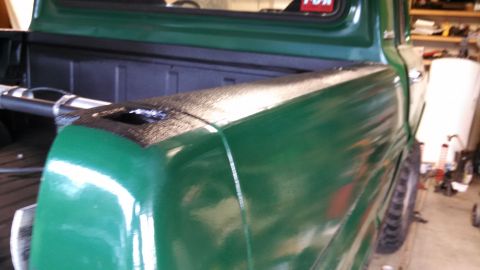 1967 Ford F-250 - The side of a green 1967 Ford F-250 pickup truck bed is visible, with a red sticker on the rear window.
