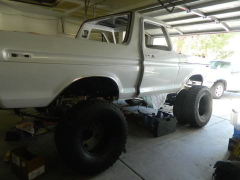 1979 Ford Bronco - White 1978 Ford Bronco body undergoing restoration in a garage with large tires. Another vehicle is parked behind.