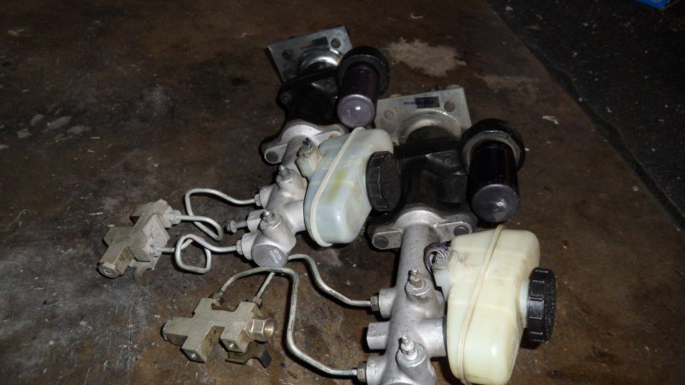 Several brake master cylinders with plastic reservoirs and metal lines on a dark surface