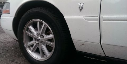 2000 Mercury Grand Marquis - Close-up of a white car's side fender and wheel, a V8 emblem.