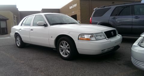 2000 Mercury Grand Marquis - A white sedan is parked in front of an Auto Center with a gray SUV behind it.