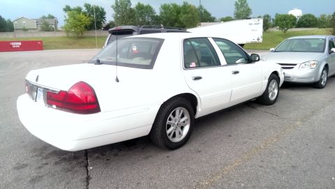 2000 Mercury Grand Marquis - A white sedan is parked in a lot next to another vehicle, with a trailer in the background.