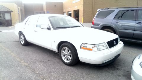 2000 Mercury Grand Marquis - A white sedan is parked in a lot next to a grey SUV, with a portion of another vehicle visible in the foreground.
