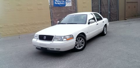 2000 Mercury Grand Marquis - White 2000 Mercury Grand Marquis sedan parked on asphalt with a building in the background.