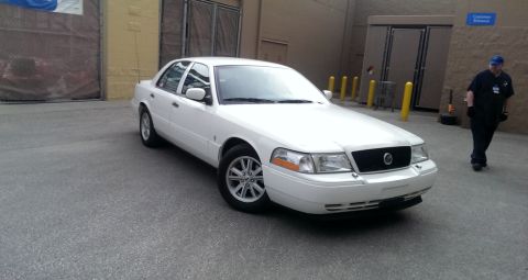 2000 Mercury Grand Marquis - A white sedan is parked in an outdoor lot with a person walking in the background.