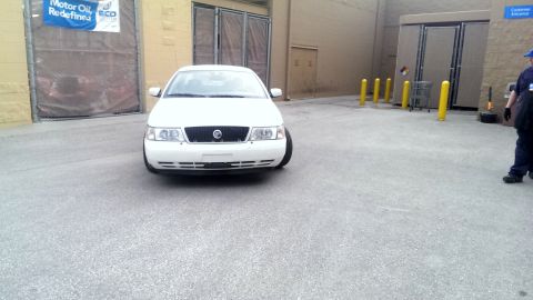 2000 Mercury Grand Marquis - A white 2000 Mercury Grand Marquis is parked in front of a building with yellow bollards.