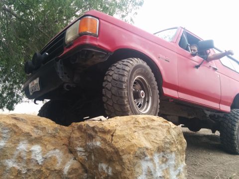 1988 Ford Bronco - This red SUV is navigating over large rocks on an off-road trail.