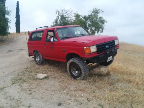 1988 Ford Bronco - A red Ford Bronco is parked on a dirt hill, its tires elevated by rocks.