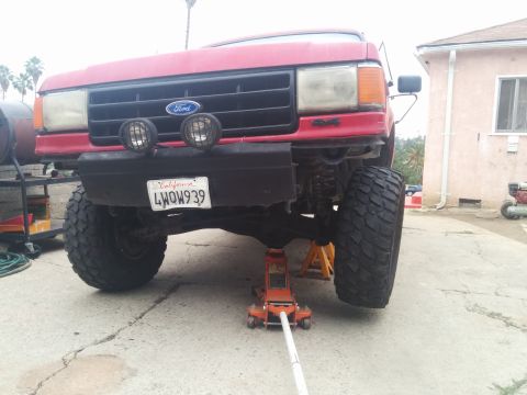 1988 Ford Bronco - This red Ford truck is being worked on, lifted by a jack and resting on jack stands.