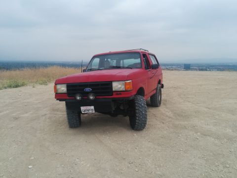 1988 Ford Bronco - This red 1988 Ford Bronco is parked on a dirt hill, its off-road capabilities with large tires.