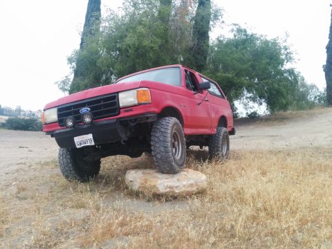 1988 Ford Bronco - Red 1988 Ford Bronco with aftermarket bumper and lights, positioned on a rock.