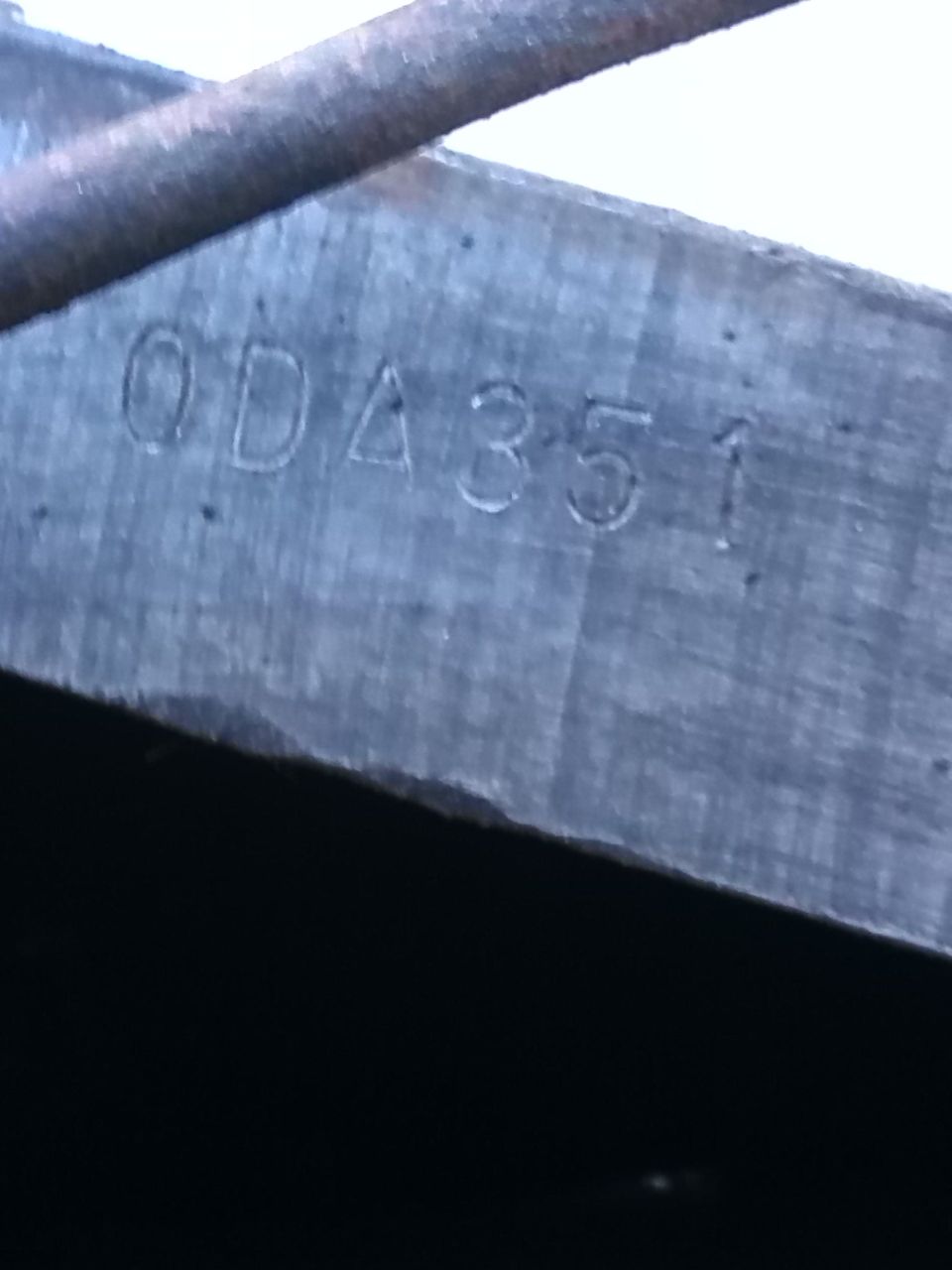 Metal plate with stamped characters '0DA351' and a partial diagonal bar