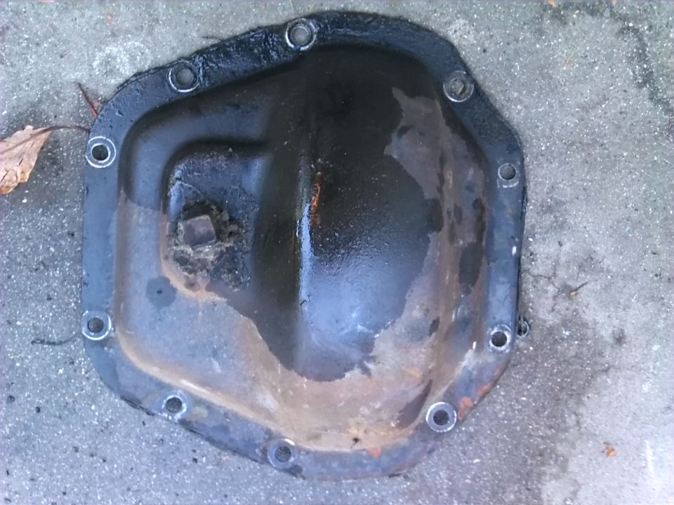 Differential cover with rust and oil residue, bolted to a concrete surface