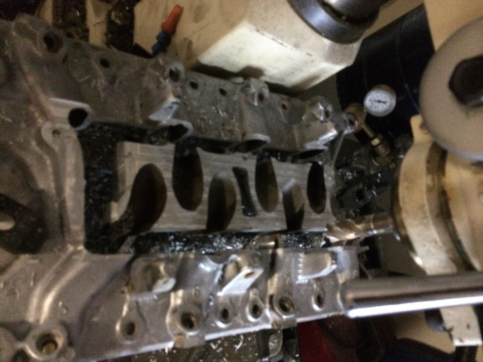 Engine block on a milling machine, metal shavings visible. A pressure gauge is attached