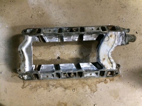 1996 Ford Bronco - Aluminum supercharger intake manifold with internal fins and mounting holes, lying on a concrete floor.