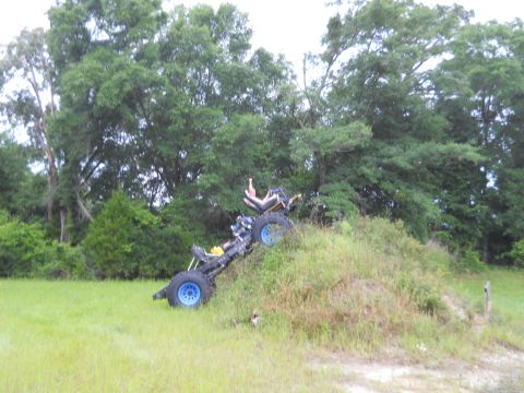 1992 Ford Bronco - An off-road vehicle is tilted on a grassy incline with trees behind it.