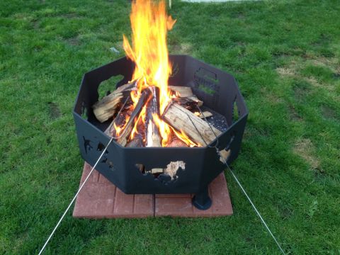 1978 Ford Bronco - A black, octagonal fire pit with decorative horse cutouts sits on brick pavers in a grassy yard, with a fire burning inside.