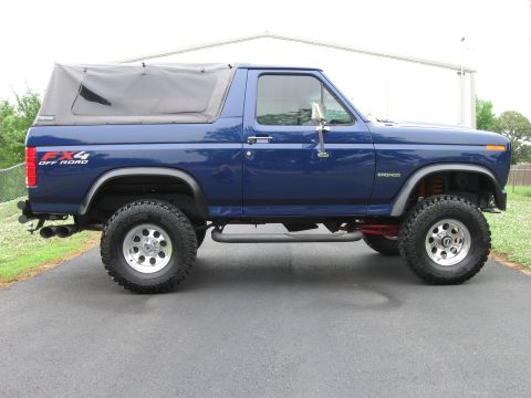 1982 Ford Bronco - A blue Ford Bronco with a soft top and lifted suspension is shown from the side.