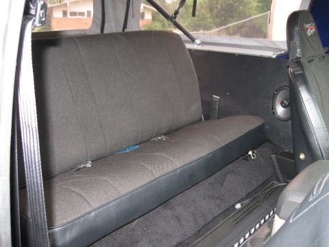 1982 Ford Bronco - The interior of a vehicle shows a rear bench seat and a speaker mounted on the side panel.