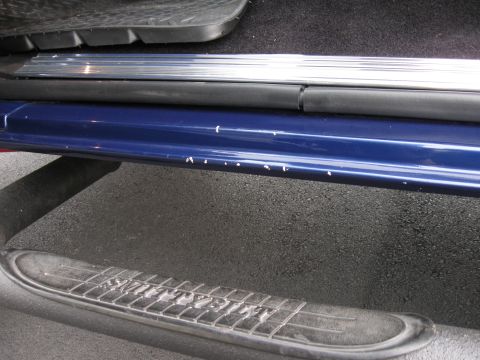 1982 Ford Bronco - Close-up of a blue vehicle's door sill and running board, showing minor paint damage.
