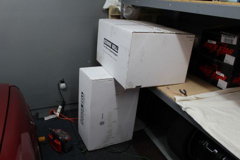 2003 Ford Crown Victoria - White Kenne Bell supercharger boxes stacked on a shelf next to a red car and Race Star boxes in a garage.