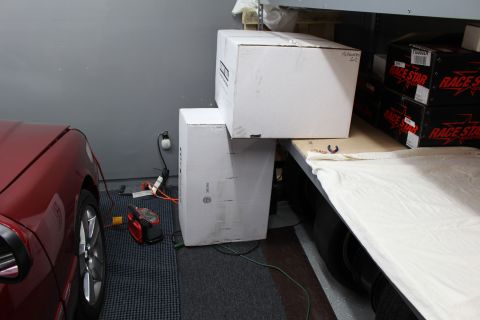2003 Ford Crown Victoria - red car parked beside stacked white boxes and shelving holding Race Star product boxes in a garage.