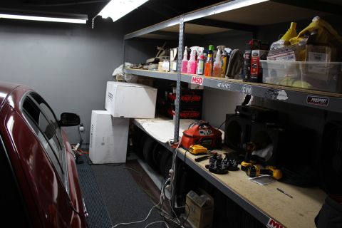 2003 Ford Crown Victoria - garage workbench and shelving stocked with cleaning supplies, tools, and boxes next to a dark red car.