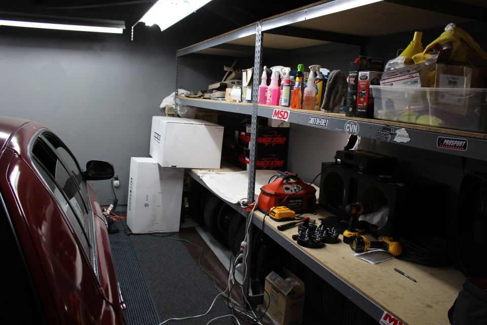 Garage shelving with cleaning supplies, tools and boxes beside a red car
