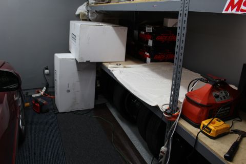 2003 Ford Crown Victoria - White cardboard boxes stacked beneath a garage shelf holding Race Star boxes, with a red car at left.