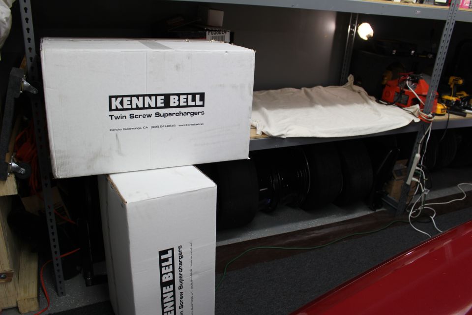 Kenne Bell Twin Screw Supercharger boxes on a shelf above black tires