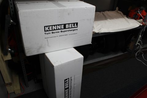 2003 Ford Crown Victoria - Two white Kenne Bell Twin Screw Supercharger boxes stacked on a garage shelf with tools and tires behind.