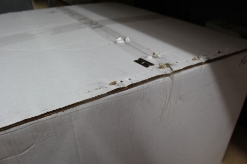 2003 Ford Crown Victoria - Top surface of a large white corrugated box with creased seams, torn edges, and a faint stamped marking.