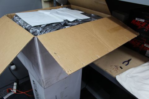 2003 Ford Crown Victoria - open cardboard box revealing white paper over dark plastic, set in a shop beside red-labeled boxes.
