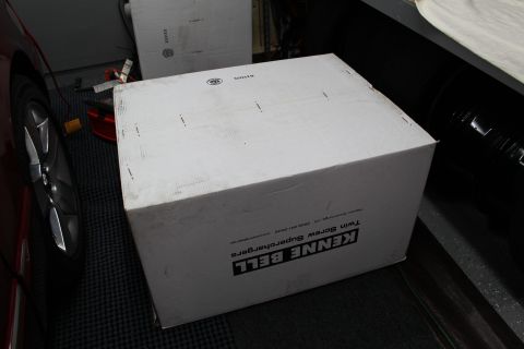 2003 Ford Crown Victoria - large white box labeled Kenne Bell Twin Screw Supercharger rests near a red car's wheel in a garage.