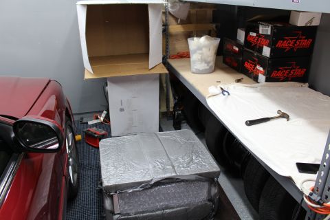2003 Ford Crown Victoria - workshop with a red car, a foil-wrapped package on the floor, tires, and Race Star wheel boxes on a shelf.