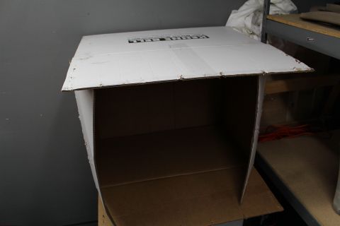 2003 Ford Crown Victoria - emptied corrugated box with flaps open sits on a shop shelf against a gray wall.