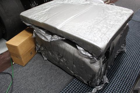 2003 Ford Crown Victoria - package wrapped in silver foil and gray plastic, taped at the base, rests on checkered shop matting.