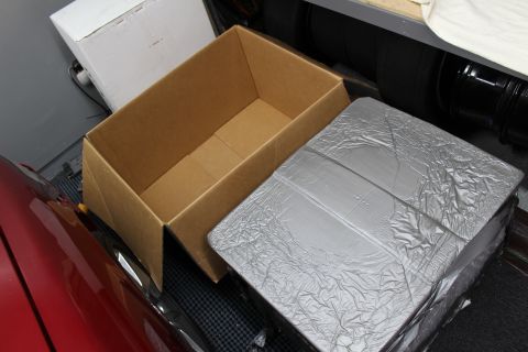 2003 Ford Crown Victoria - silver foil-wrapped block sits beside an empty open cardboard box, next to a red car in a garage.