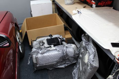 2003 Ford Crown Victoria - black-topped Kenne Bell supercharger unit unwrapped from bubble-wrap padding beside a box and red car.