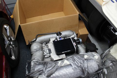2003 Ford Crown Victoria - black-topped Kenne Bell supercharger unit rests on foil packing beside its cardboard box and a wheel.