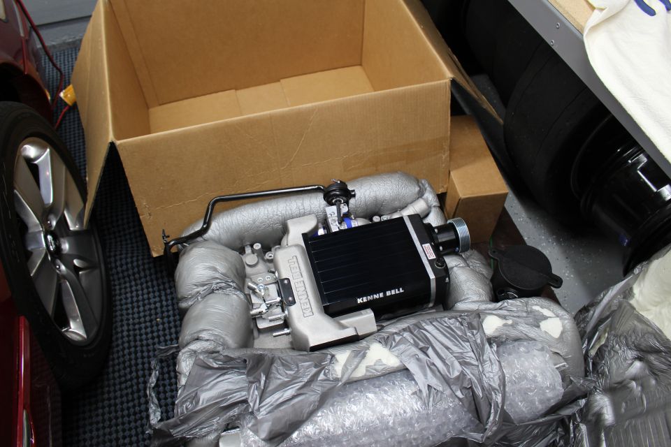 Kenne Bell supercharger unit unboxed on packing material near a wheel and box