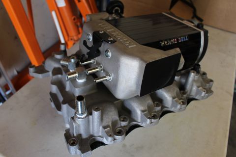 2003 Ford Crown Victoria - angled view of a Kenne Bell supercharger and manifold showing intake runner ports and mounting studs on a bench.