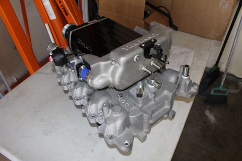 2003 Ford Crown Victoria - Kenne Bell supercharger and aluminum manifold fitted with blue silicone couplers and a paper sheet rest on a workbench.