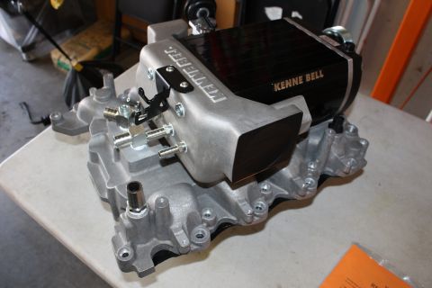 2003 Ford Crown Victoria - black intercooled supercharger unit branded Kenne Bell sits atop a cast-aluminum manifold base on a shop counter.