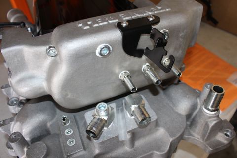 2003 Ford Crown Victoria - close view of a cast-aluminum supercharger manifold showing a black mounting bracket, protruding nipples and threaded silver fittings.